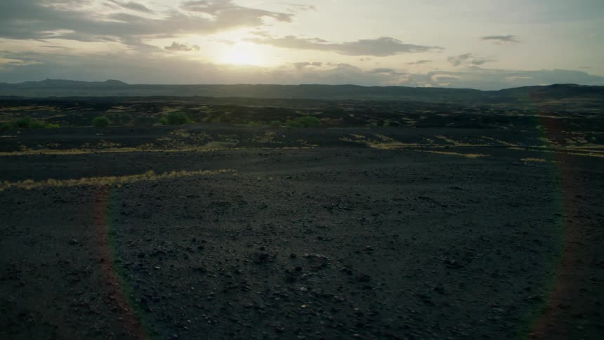 Sun shines behind clouds over grassy muddy flat land