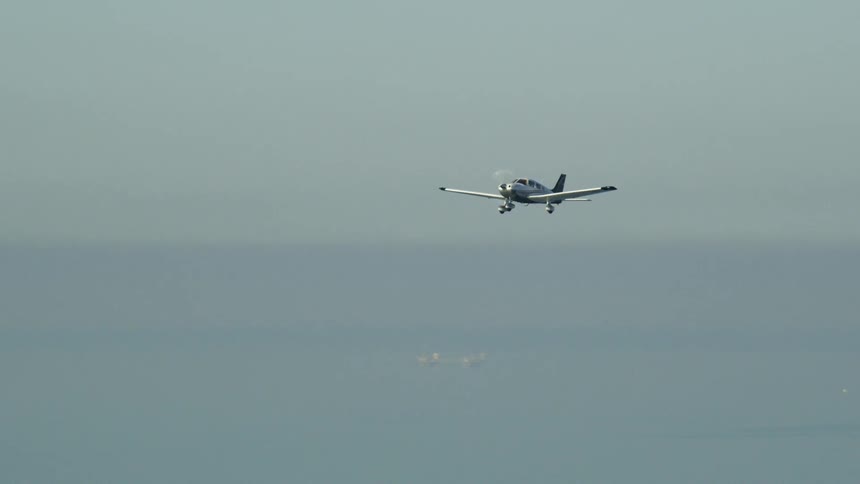 A small plane flies over the water