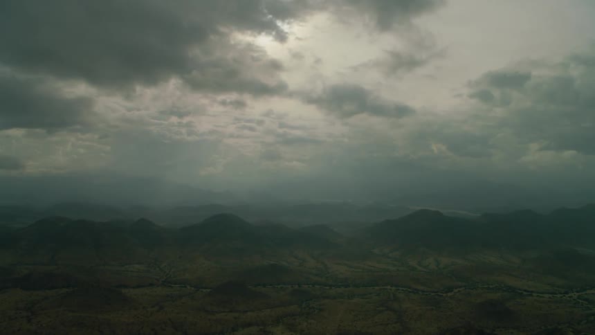 Sun shines behind clouds over hilly land
