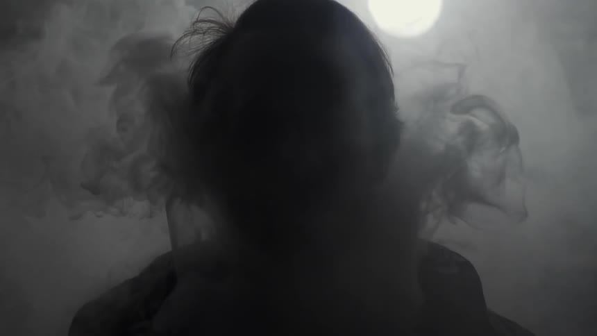 Smoke rises from below and surrounds a mans face