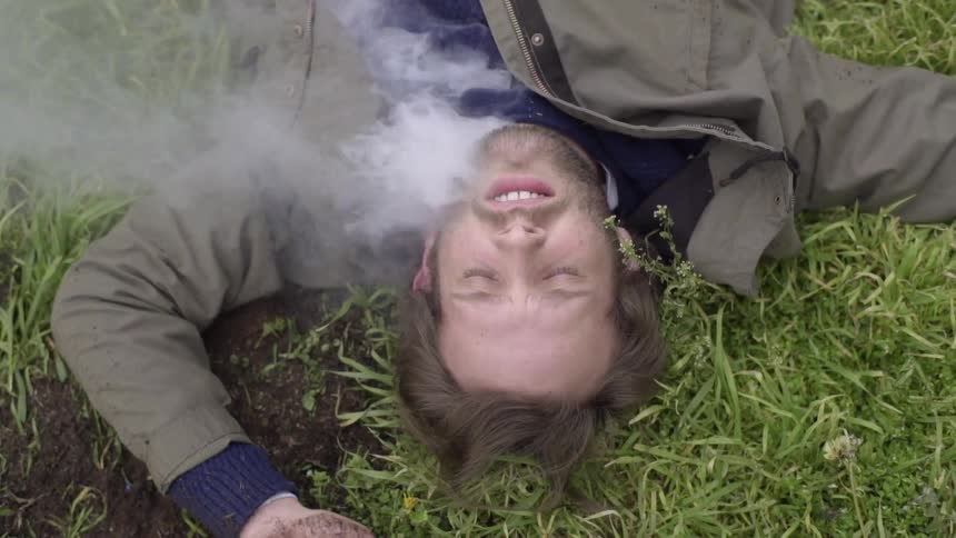 Smoke emerges from a man's jacket as he lays on the ground