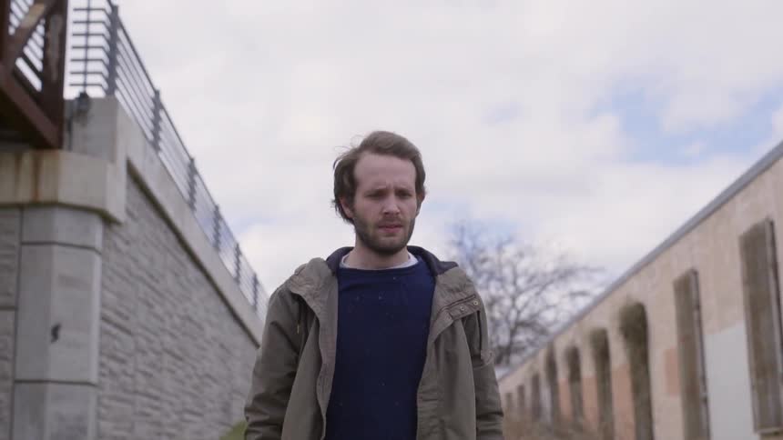 Man walking between two stone walls under a cloudy sky