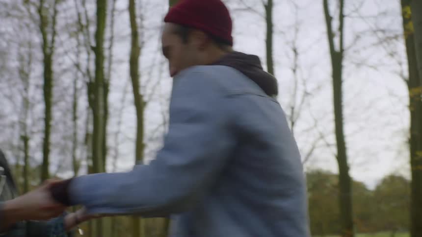 Man and woman hold hands spinning in a circle in the woods