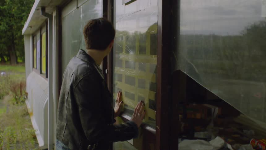 Woman looks through a taped window into a building