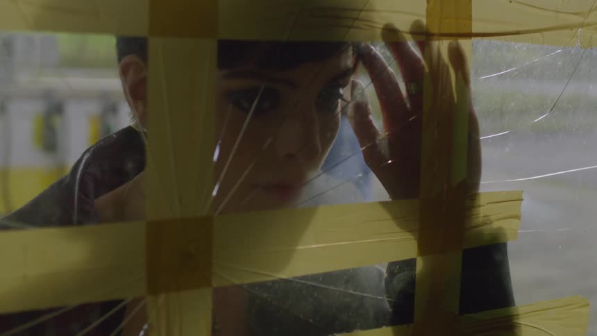 A woman is looking in through a taped up window in daylight