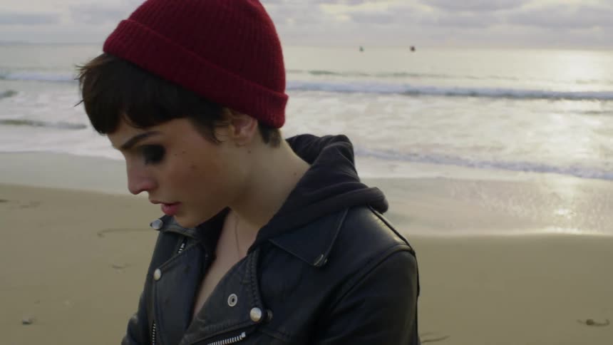 Woman stands on the beach smoking a cigarette