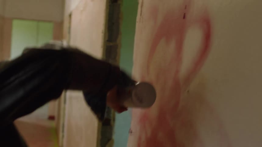 Woman spray paints a wall in a hallway