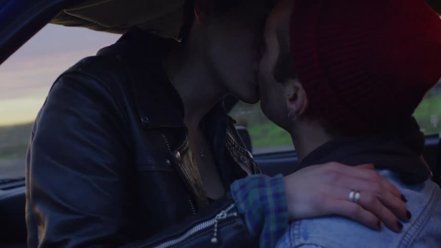 Woman sits on man's lap in car and they kiss