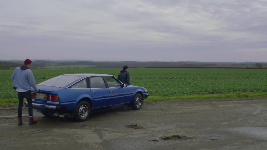 Two men stand and walk around a car