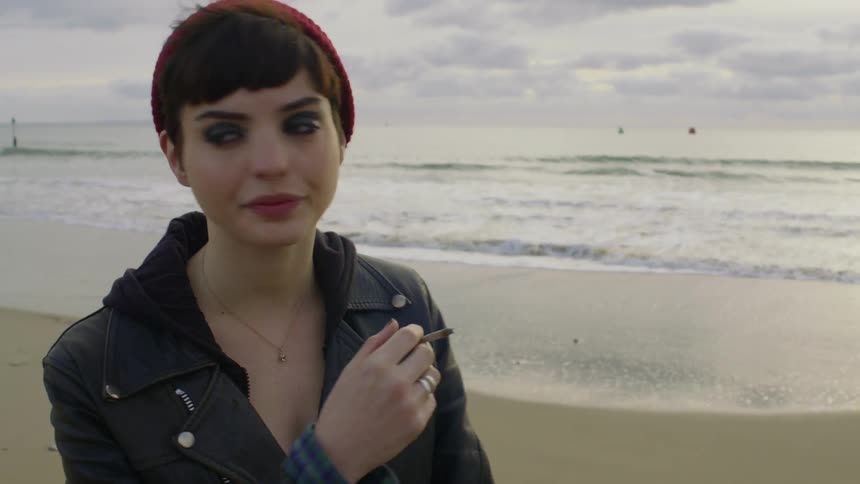 A woman is smoking a cigarette on the beach