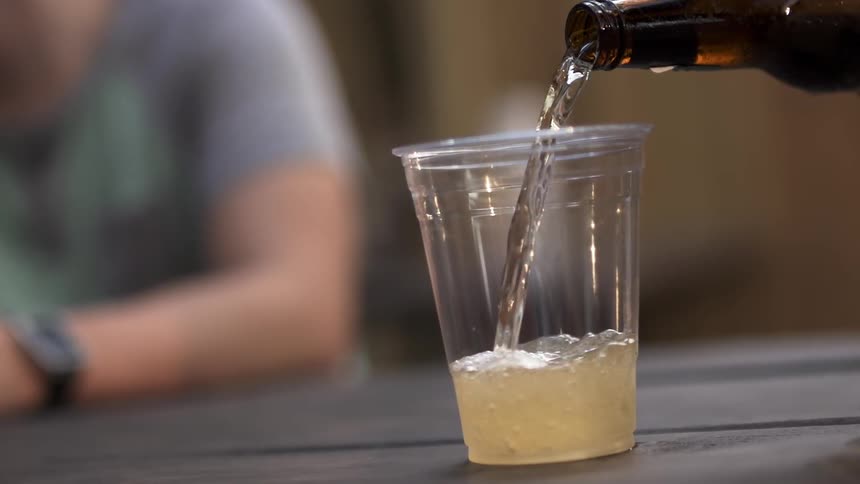 Person pouring beer into a plastic cup as another looks on
