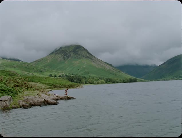 People walking out on a jetty near green mountains on a cloudy day