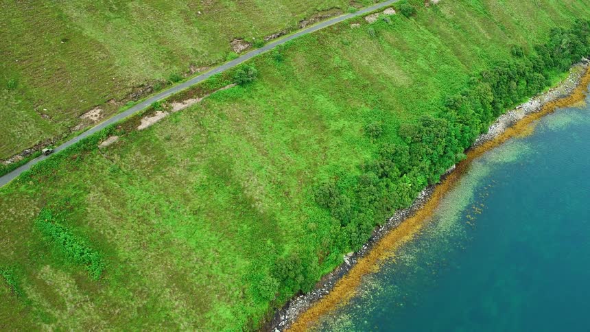A vehicle is driving on a road above a coastline during the day
