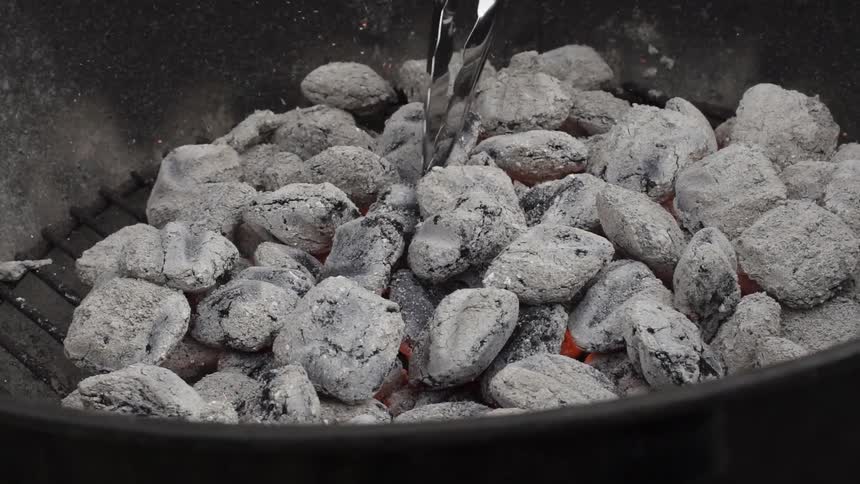 Tongs jostle white coals in a grill