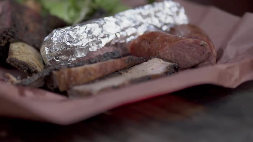 A person drops a plate of barbecue and grilled food on a table