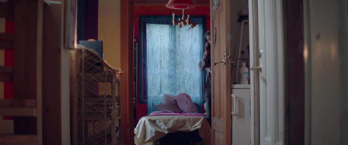 A view down a hallway shows an empty bed with pink pillows indoors.