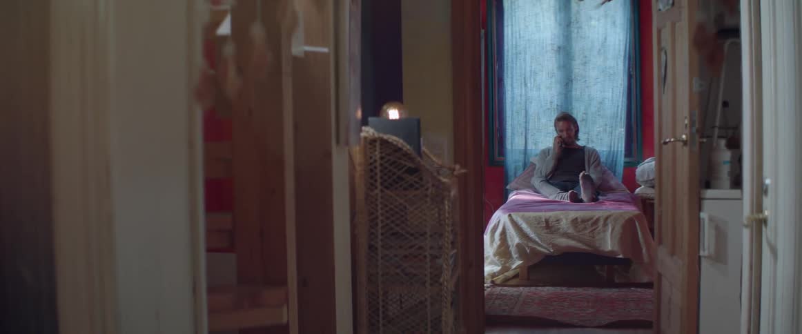 A young guy sits comfortably on an unmade bed during a phone call.
