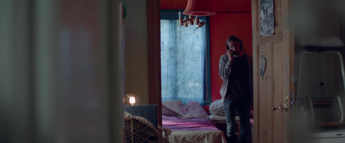 Man sits on bed talking on cell phone then gets up as he continues to talk