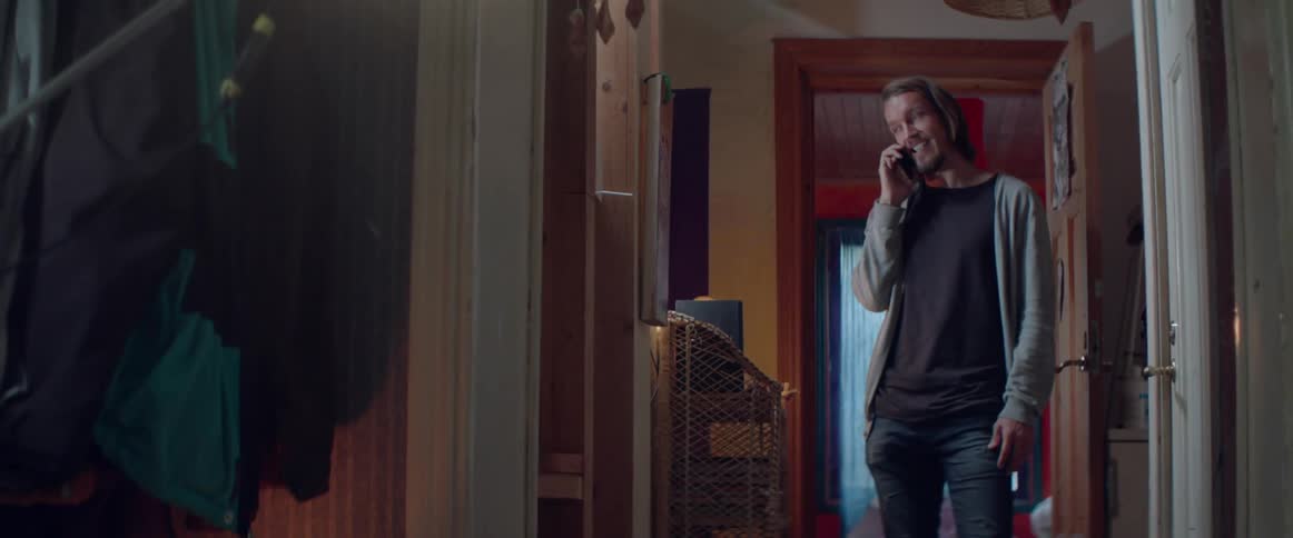 An expressive person enjoys a pleasant telephone conversation near a bedroom hallway inside.