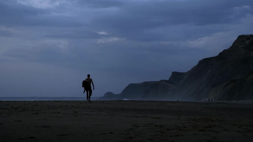Man walks down a beach carrying a backpack