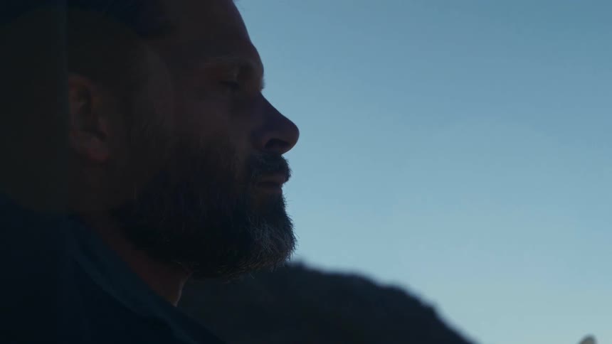 Bearded man raises his arms and pulls a turtle neck over his head