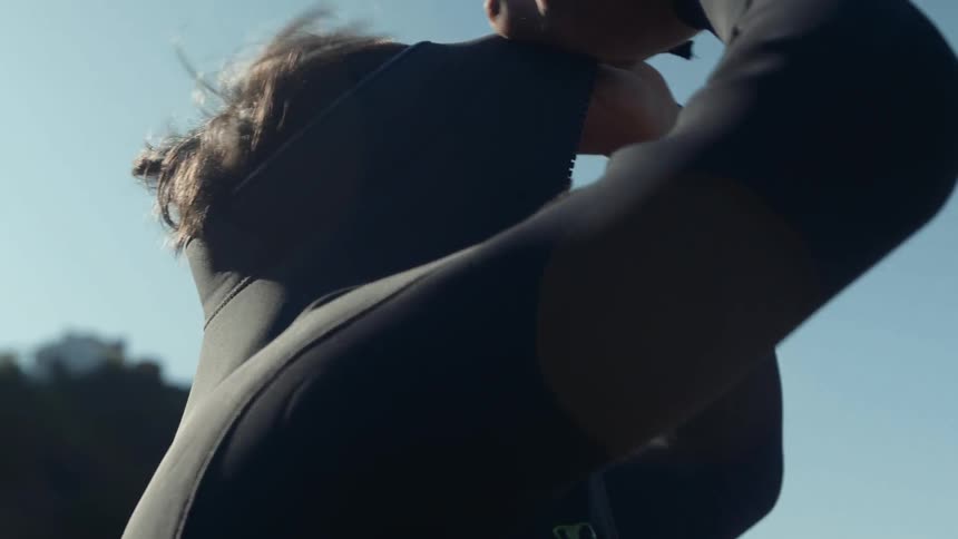 A man pulls the top of his wetsuit over his head and secures it