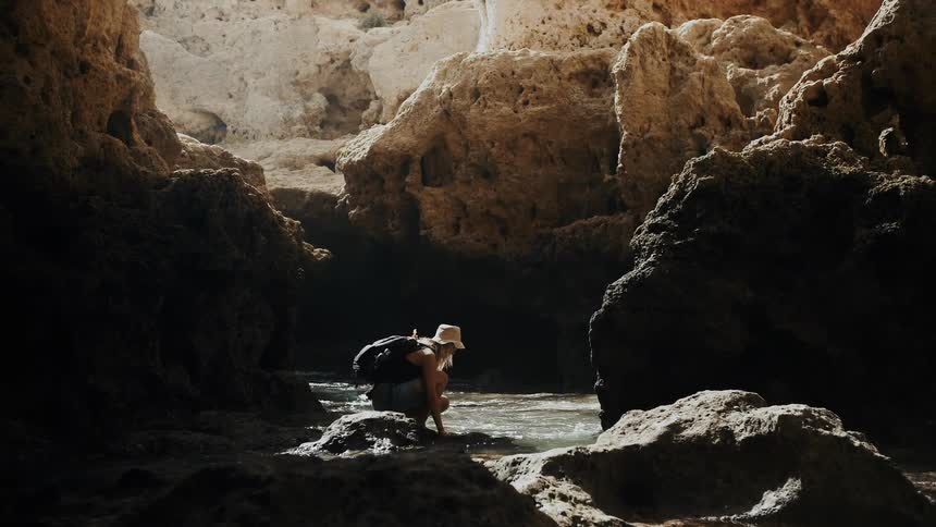 A woman crouches next to ocean water on a beach