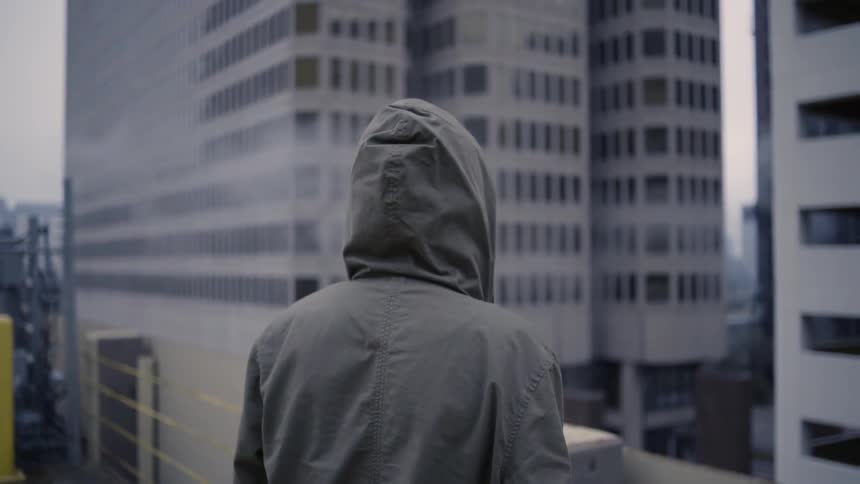 A man in a jacket stands on a rooftop and observes the city