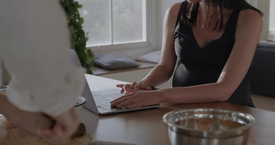 A woman works on the laptop as a man prepares food