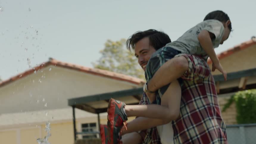 Man holding a child on his shoulder plays with a hose