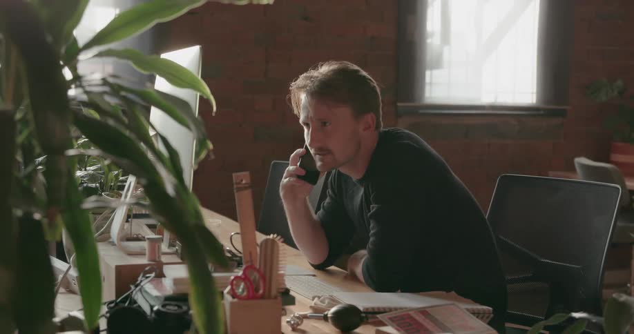 A man leans forward talking on the phone at his desk