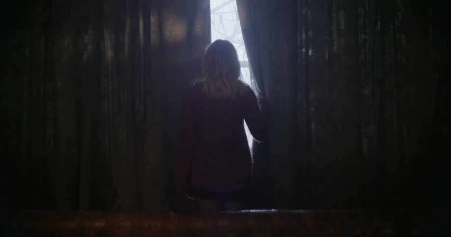 A woman pushes back the curtains and looks out the window