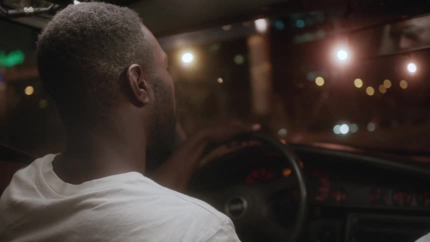 A man is driving a car at night in a city