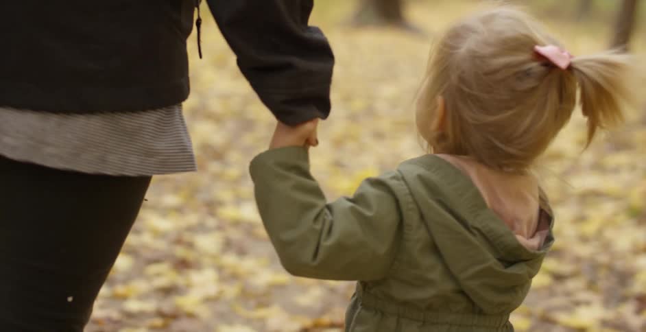 A woman and young girl hold hands in a forest