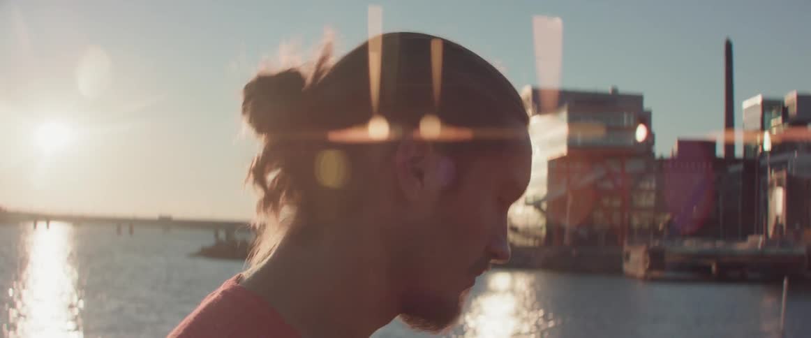 Close up of a man looking down while walking along waterfront at sunset.