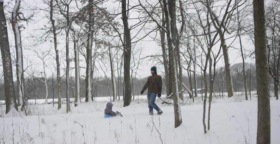 A man pulls a child on a sled through the forest