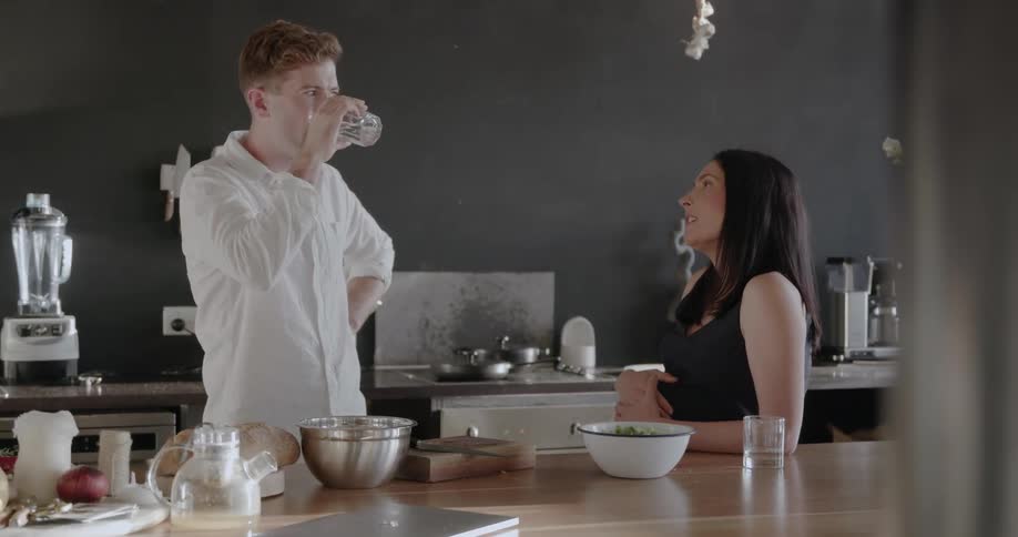 A man takes a drink as he talks with a woman