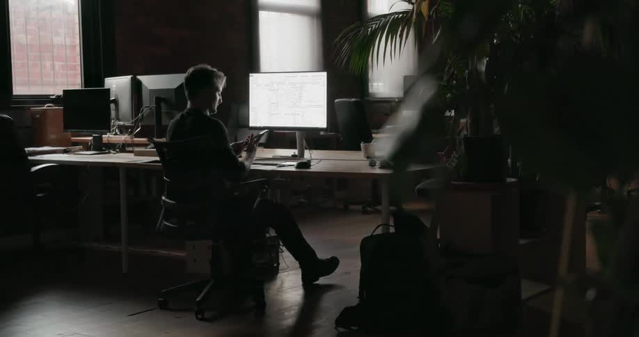 A man sits at the desk then pulls out his phone