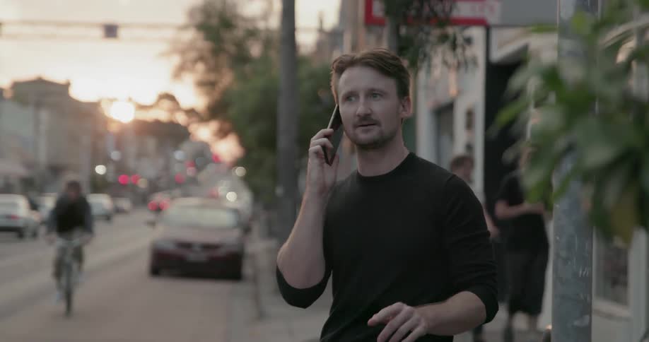 A man smiles as he talks on the phone outside
