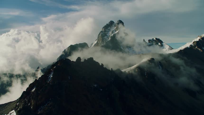 Clouds are drifting over a mountain peak in daylight