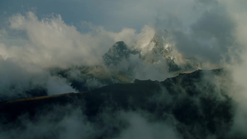 Clouds pass through and above tall mountains