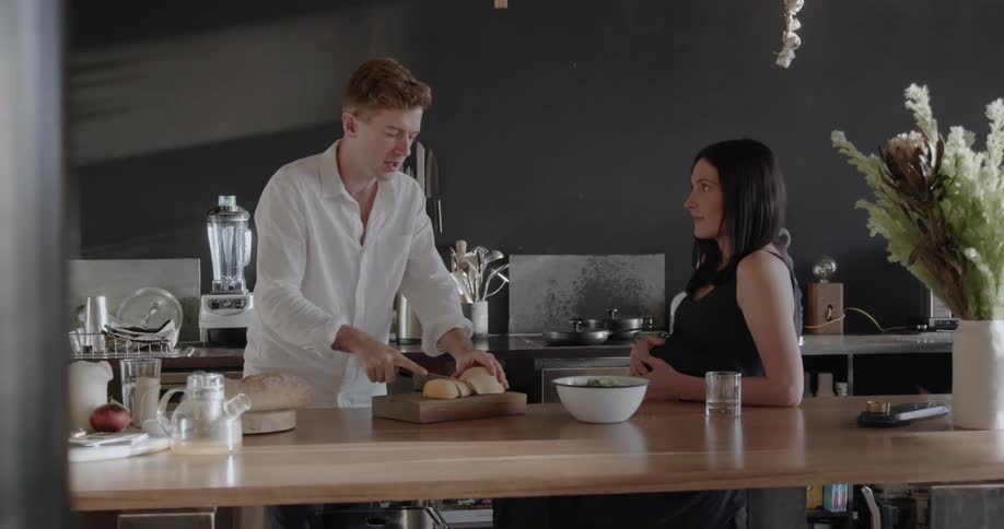 A man is cutting food as he talks with a woman