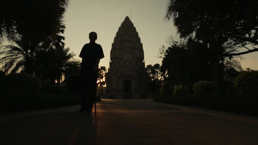 A man limps outside with a walking stick at sunset