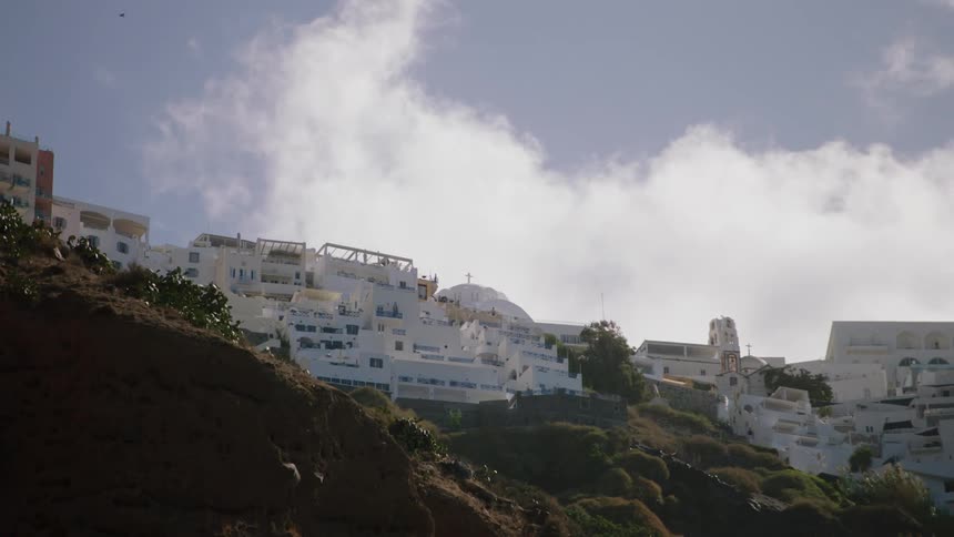 White clouds float over buildings on a mountain side