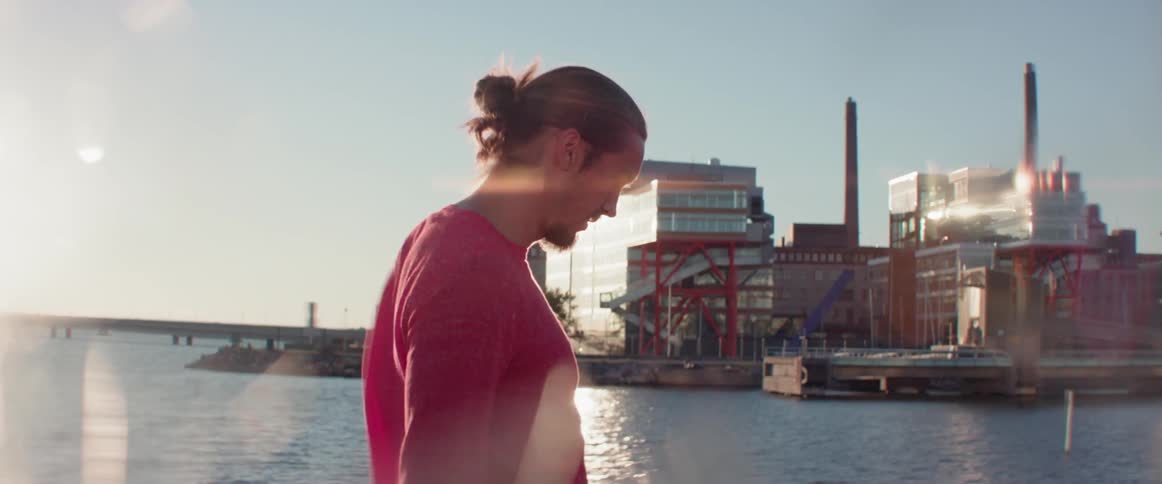 Side profile of a young man walking near the water with city buildings behind.