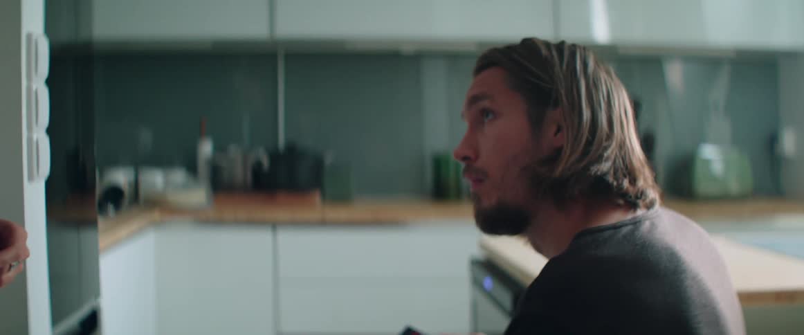 Side profile view of a serious man sitting alone inside a modern kitchen.
