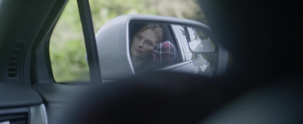 Woman leans through a window in a car as it travels down a road