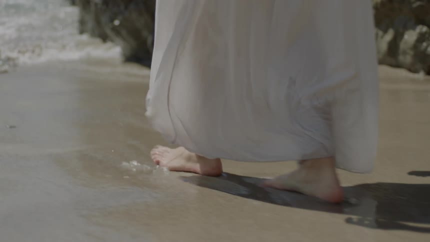 A woman in a white dress walks on the beach