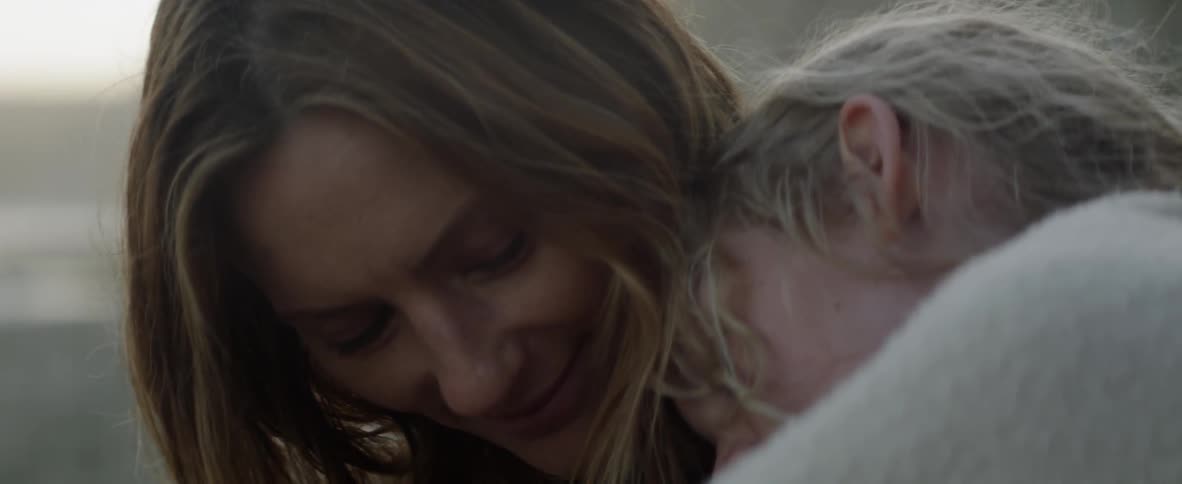 Blond woman smiles as the leans her head against a small child's head