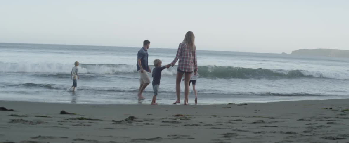 A family of five plays together at the water’s edge as waves roll in